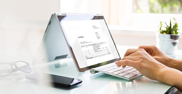 Hands re-typing invoice line items into a laptop